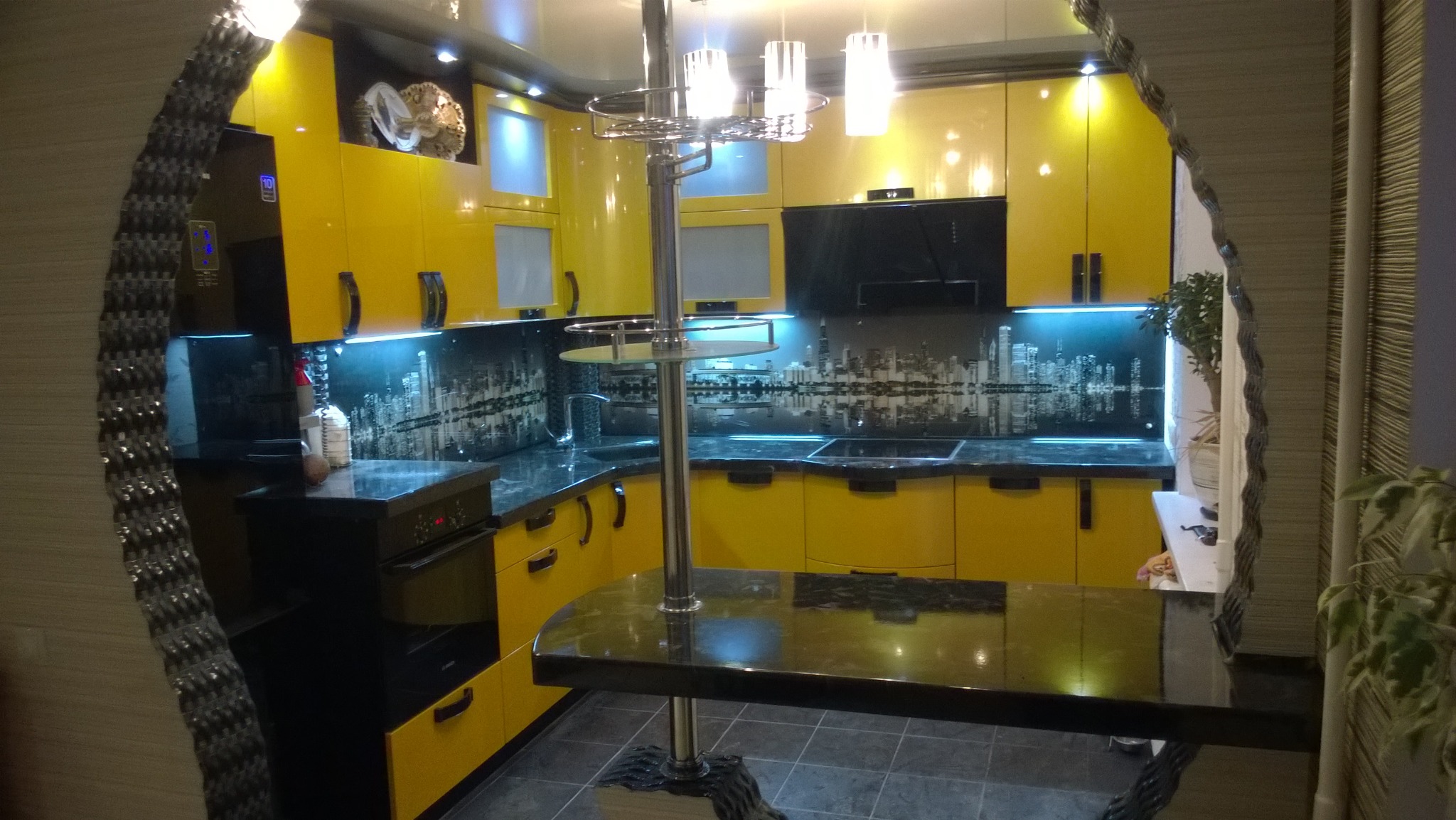 Żółta kuchnia z czarnymi blatami i motywem miasta na szklanej ściance, widoczna przez dekoracyjny otwór w ścianie. Nowoczesne oświetlenie.