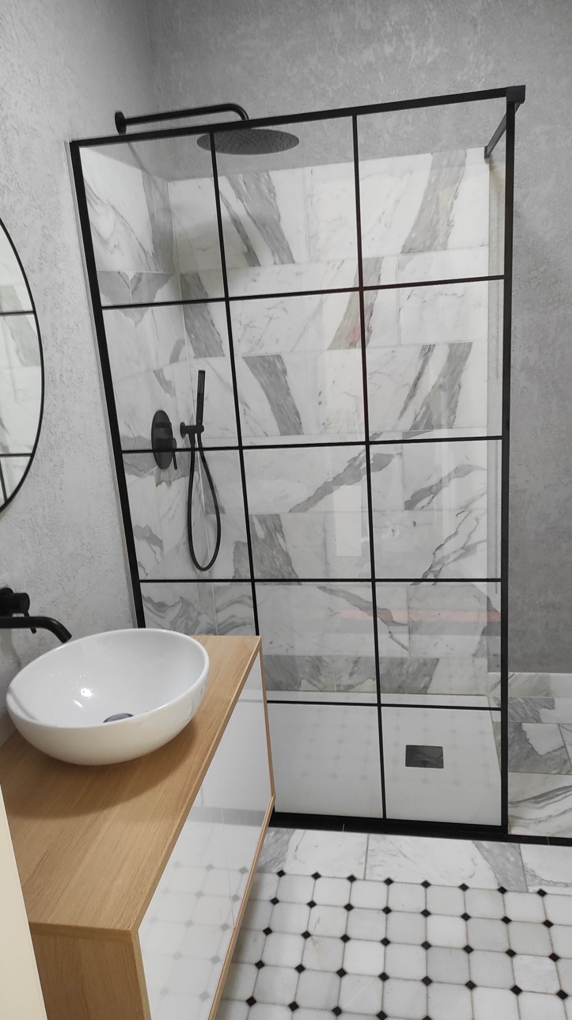 Elegancka kabina prysznicowa walk-in z czarnymi profilami i marmurowymi płytkami, umywalka nablatowa na drewnianym blacie, wzorzysta podłoga w łazience.