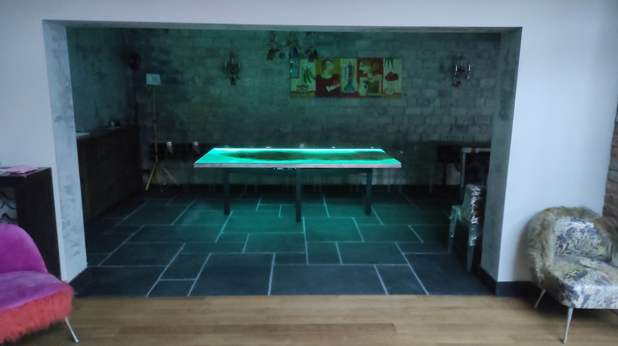 Stylowe wykończenie wnętrza w Piasecznie: podświetlany stół z żywicy epoksydowej w loftowym wnętrzu z kamienną ścianą i ciemną podłogą z płytek. Unikalny design.