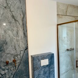 Mateusz Gąciarz - Wykończona łazienka z szarą marmurową ścianą, złotymi detalami armatury i kabiną prysznicową z marmurowym wzorem. Nowoczesny design.