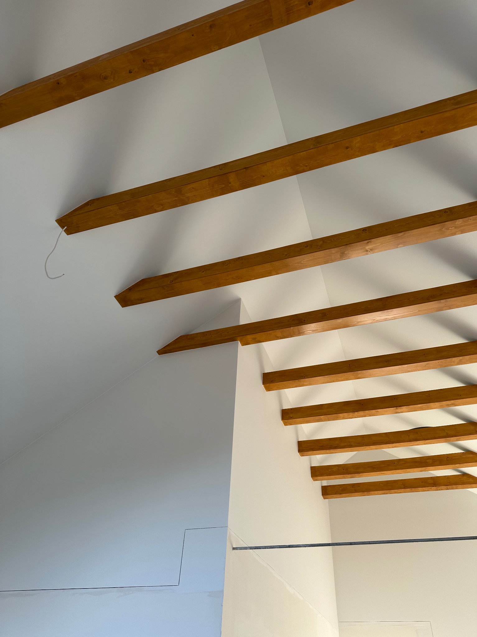 Białe wnętrze poddasza z drewnianymi belkami stropowymi, świeżo pomalowane ściany i sufit, widok z dołu.