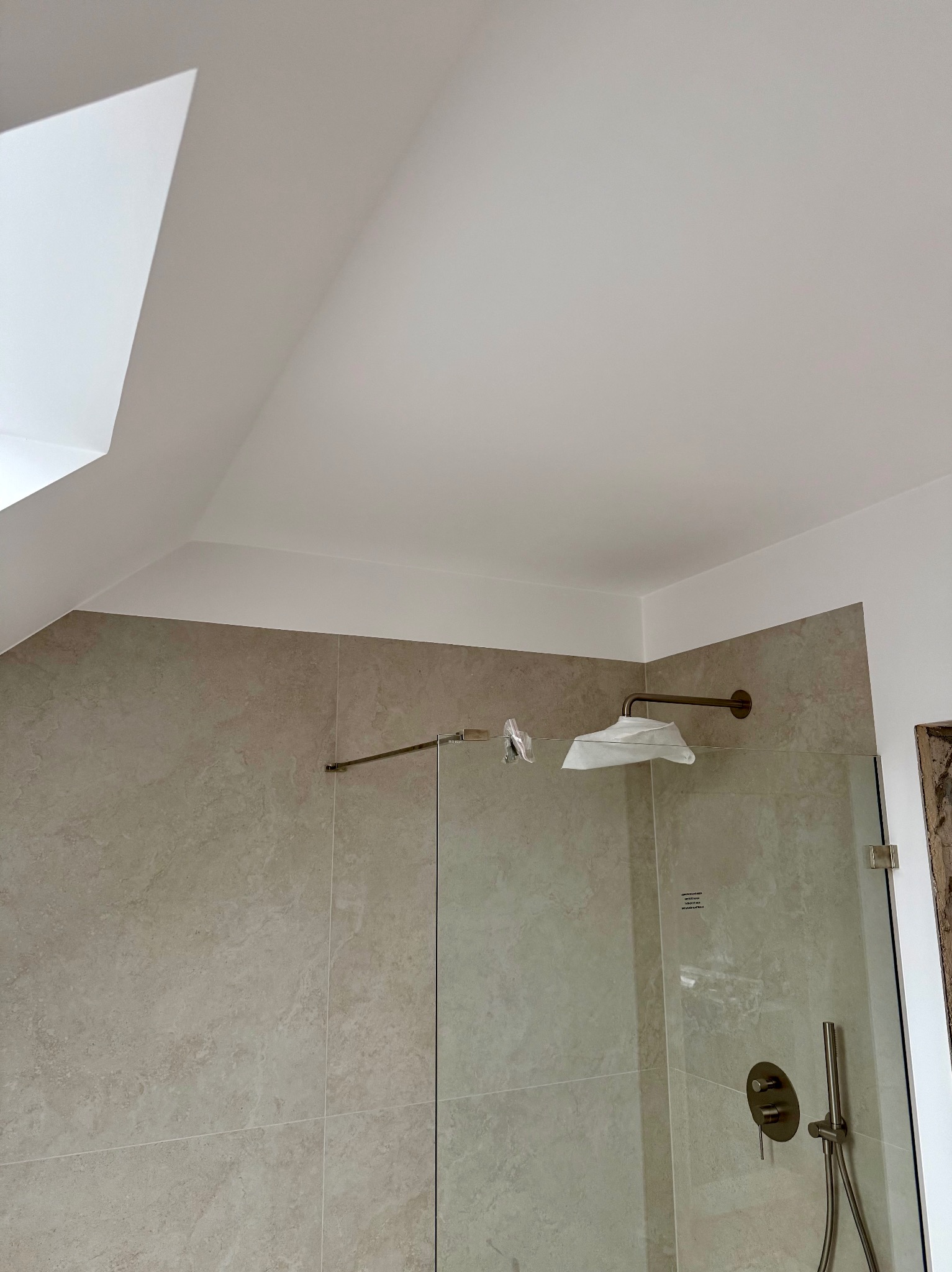 Wykończona łazienka z kabiną prysznicową w Brzesku. Beżowe płytki imitujące kamień, biały sufit ze skosem, złota armatura. Nowoczesny design.