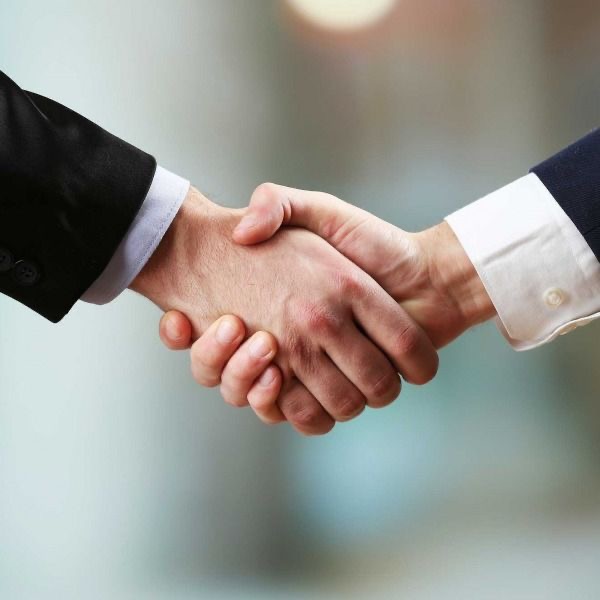 Uścisk dłoni dwóch mężczyzn w garniturach na rozmytym tle, symbolizujący porozumienie lub współpracę biznesową.