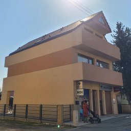 JACEK KRÓLCZYK STELLARIS - Dwukondygnacyjny budynek o nietypowej bryle z balkonami i oknami, pomalowany w odcieniach beżu i brązu, z widocznymi szyldami firm ubezpieczeniowych na parterze.