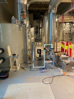 Instalacja przemysłowa z rurami, zbiornikiem i przewodami wentylacyjnymi. Widoczne elementy montażowe i narzędzia, co sugeruje etap prac instalacyjnych.