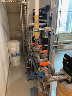 Kompleksowy system rur z zaworami w pomieszczeniu technicznym, widoczne elementy instalacji wodnej i filtracyjne, jasne oświetlenie, metalowe konstrukcje wsporcze.