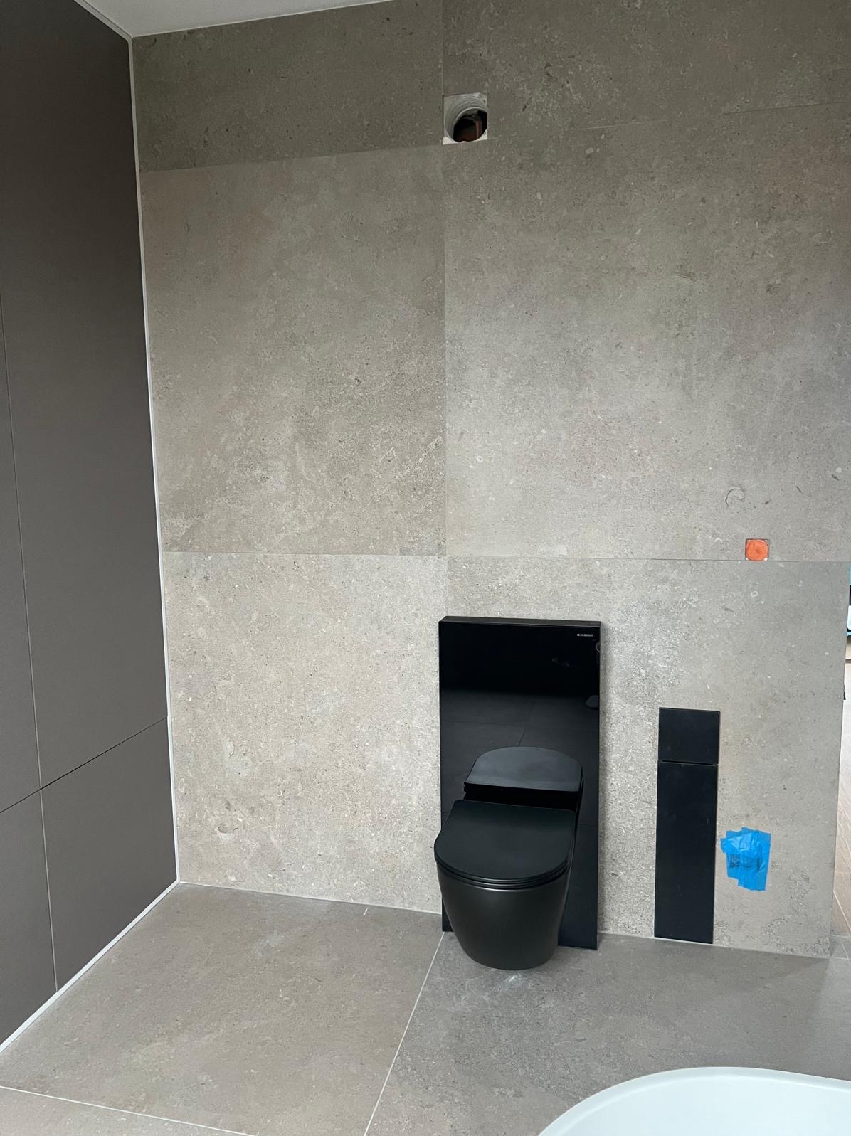 Nowoczesna toaleta w zabudowie, czarna armatura na tle szarych, wielkoformatowych płytek. Minimalistyczny design łazienki w trakcie wykańczania.