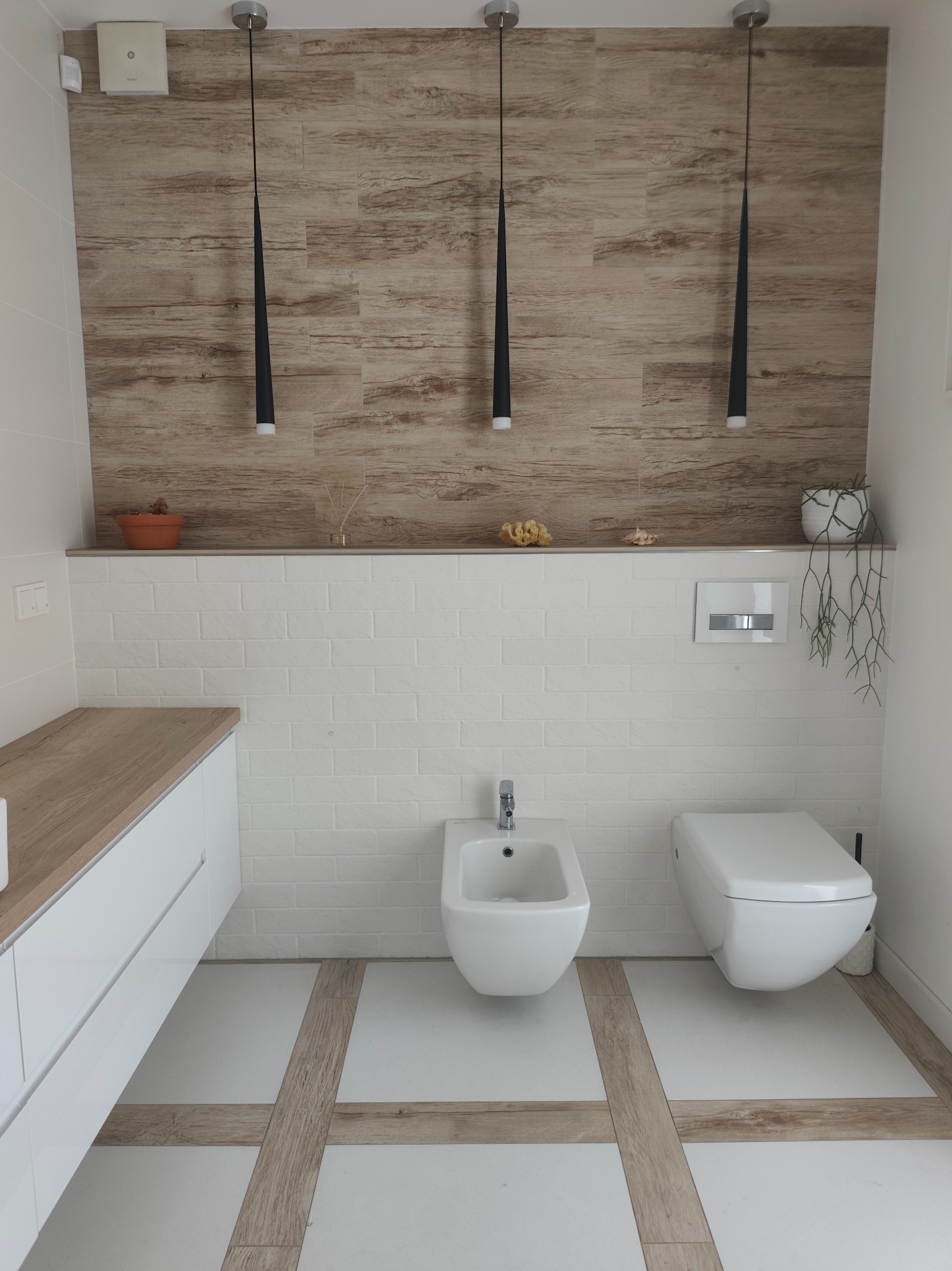 Nowoczesna aranżacja wykończenia łazienki w Olsztynie. Białe płytki, drewnopodobne akcenty na ścianie i podłodze, minimalistyczne oświetlenie.