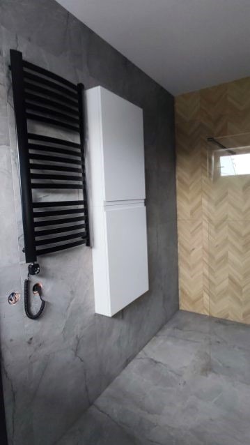 Nowoczesna łazienka: czarny grzejnik drabinkowy, biała szafka wisząca na marmurowej ścianie, drewnopodobna płytka w jodełkę na ścianie prysznica.