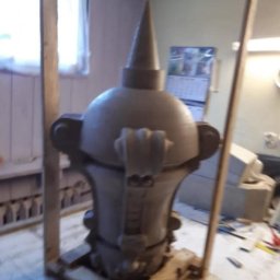 WE-NA - Szara, gliniana forma kominka z dekoracyjnymi elementami, zabezpieczona drewnianą konstrukcją, w jasnym pomieszczeniu z narzędziami na stole.