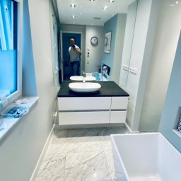 Krzysztof Ubych Usługi Budowlane - Nowoczesna łazienka z marmurową podłogą, białymi szafkami pod umywalką i dużym lustrem, w którym odbija się osoba robiąca zdjęcie.