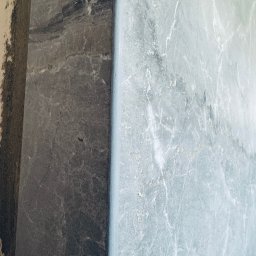 Krzysztof Ubych Usługi Budowlane - Położona płytka imitująca marmur w odcieniach szarości i błękitu, widoczny fragment ściany przed wykończeniem. Detal wykończenia wnętrza.