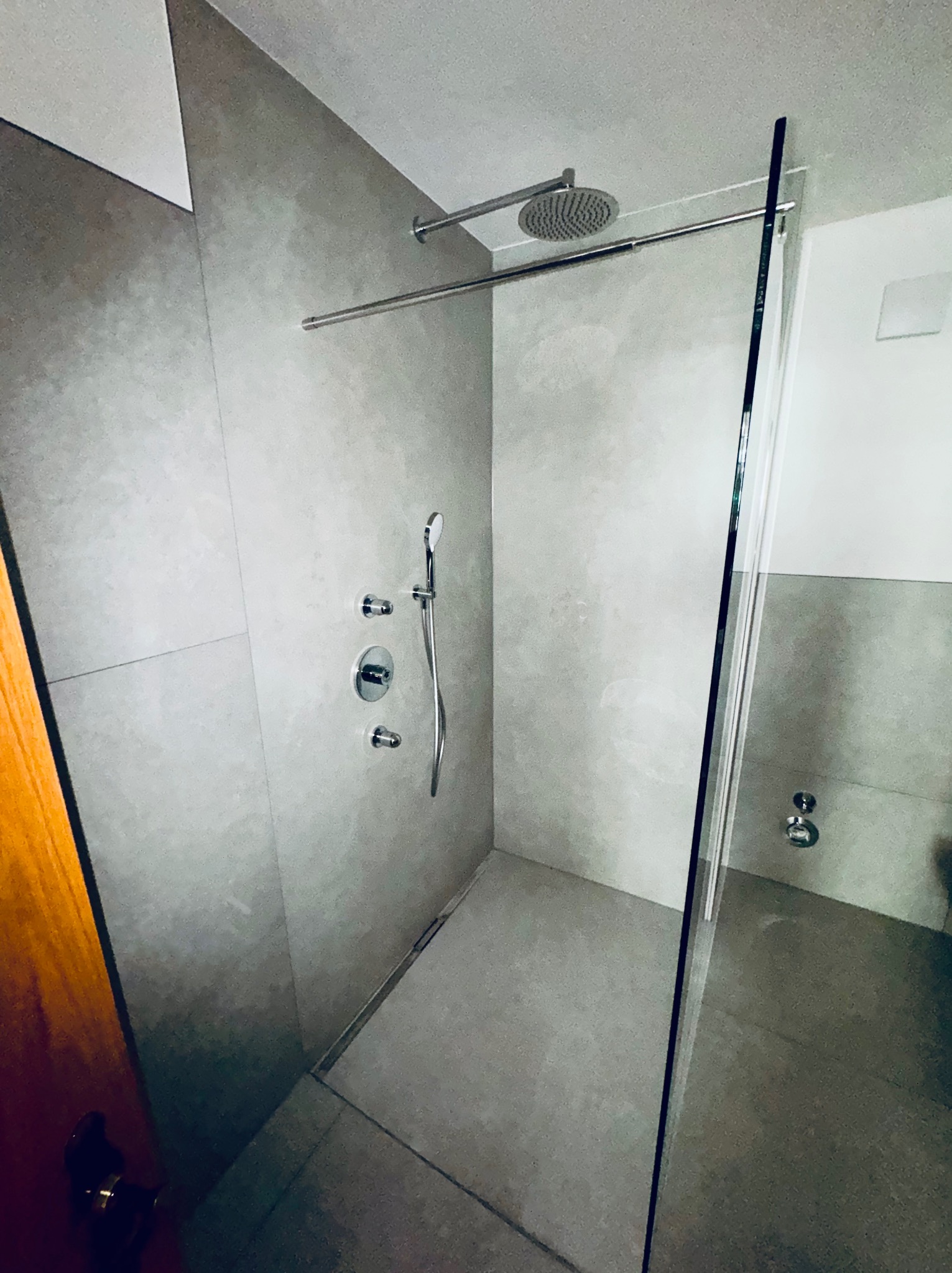 Nowoczesna kabina prysznicowa walk-in z szarymi płytkami, deszczownicą i szklaną ścianką. Minimalistyczny design, chromowana armatura, widok z boku na otwartą przestrzeń.