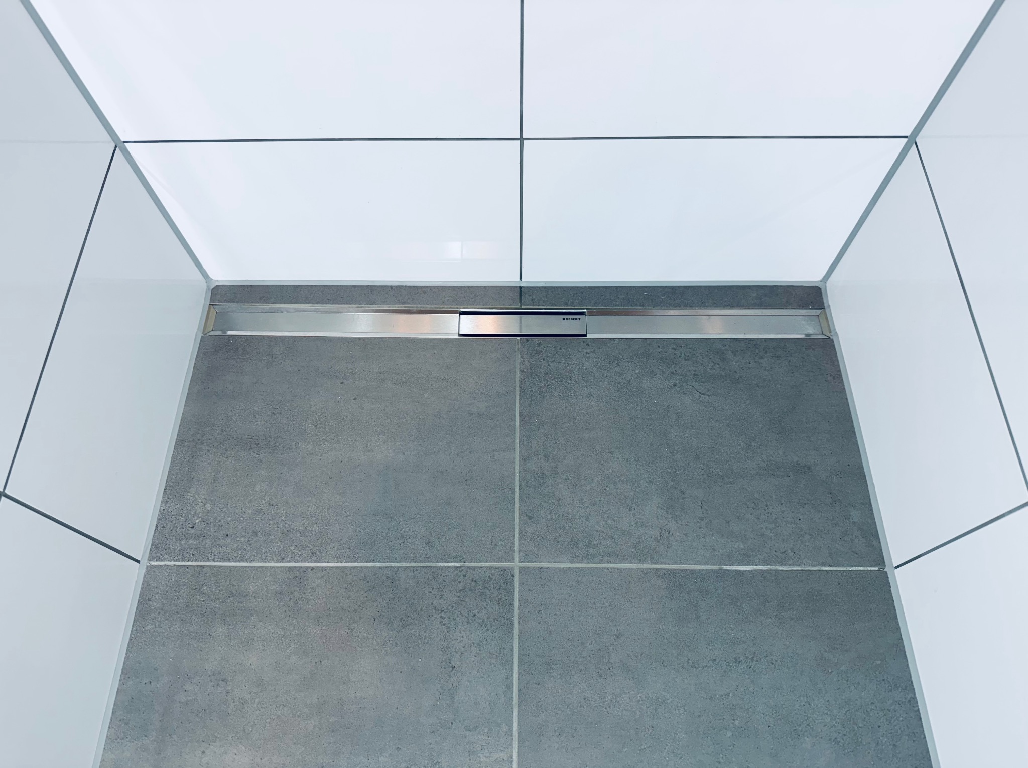 Szare płytki podłogowe i białe płytki ścienne w nowoczesnej łazience z odpływem liniowym Geberit. Minimalistyczny design.