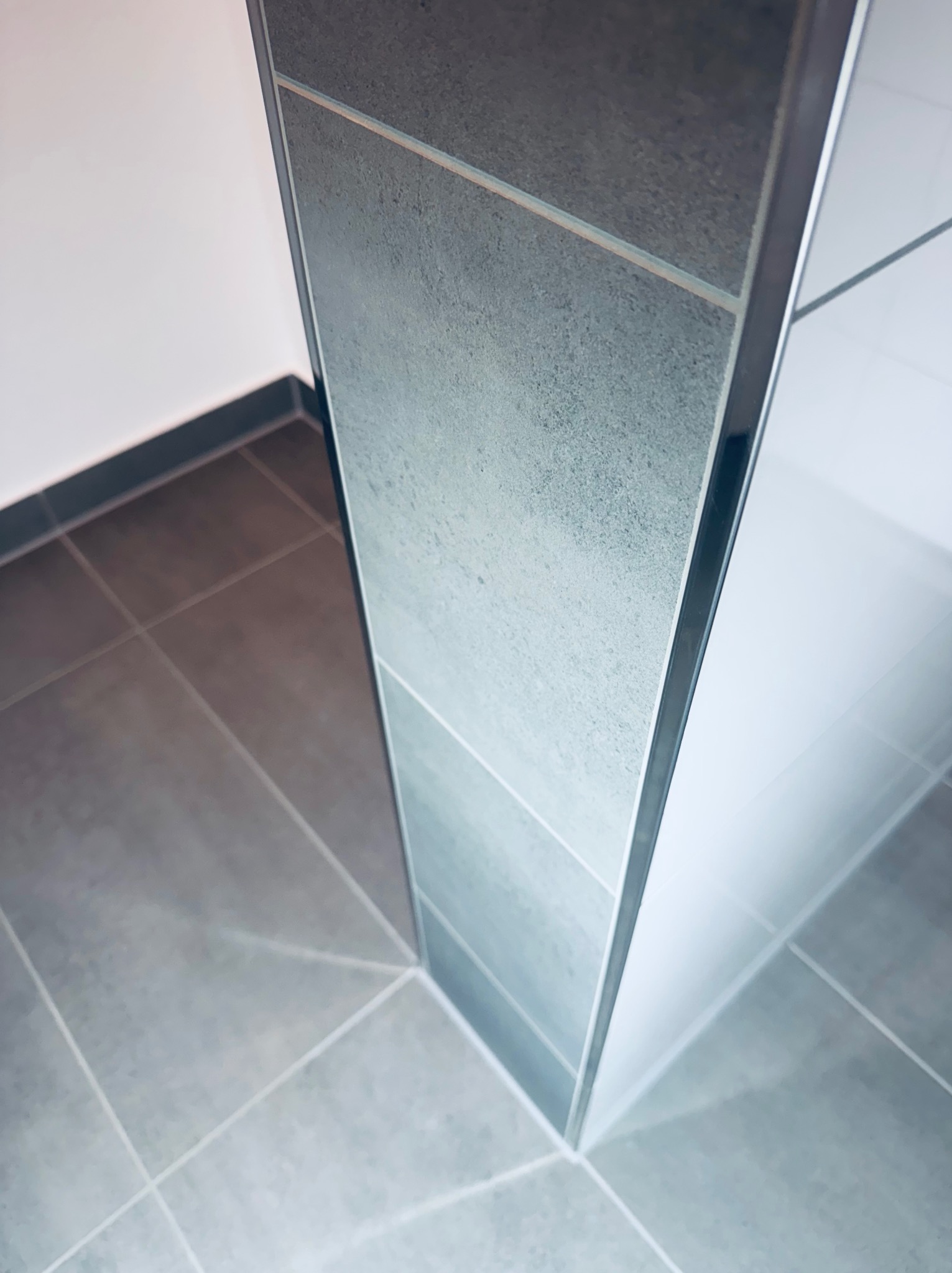 Szare płytki podłogowe i ścienne z metalową listwą wykończeniową w rogu pomieszczenia. Minimalistyczny design, nowoczesne wykończenie.