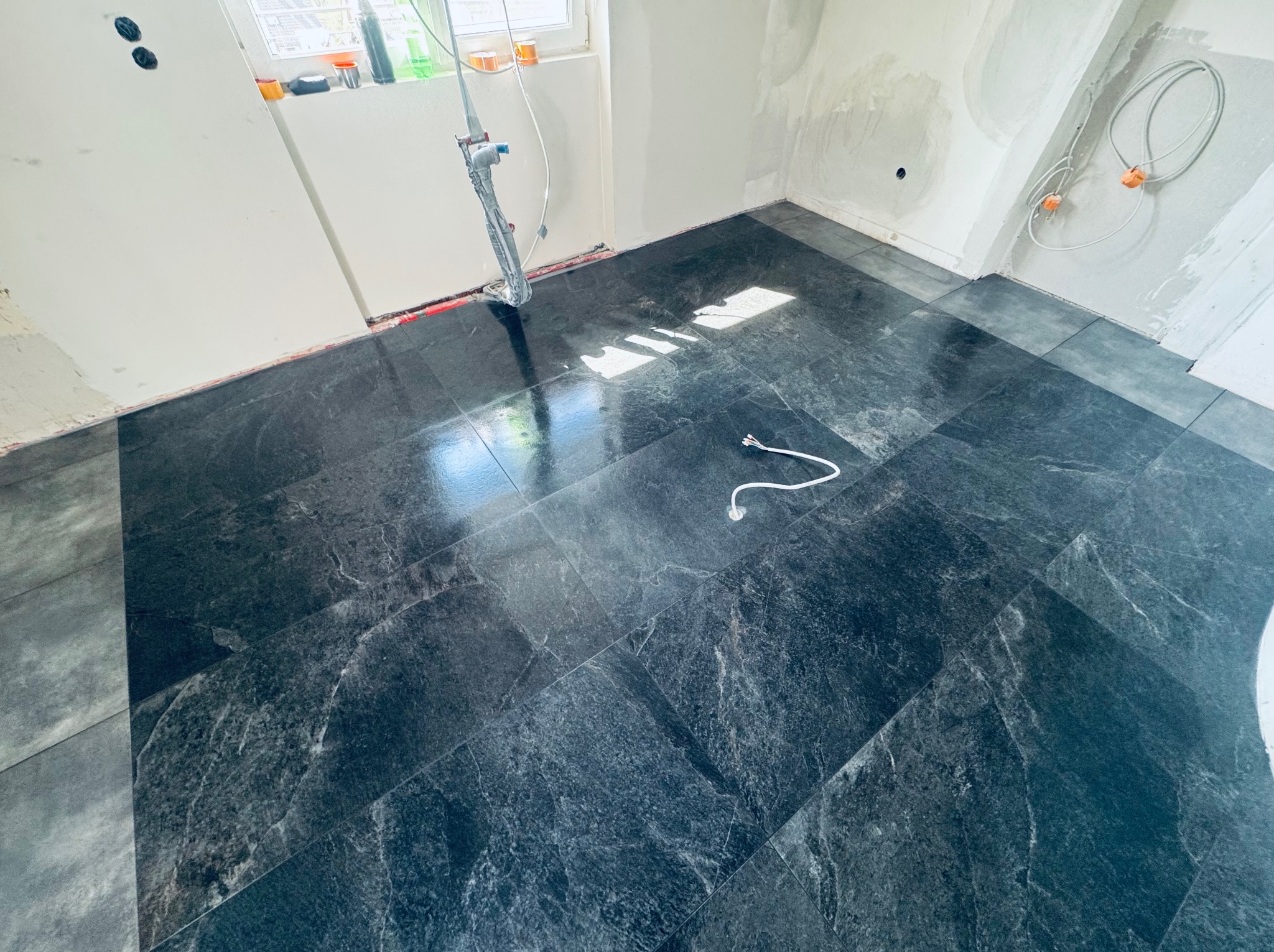 Ułożone ciemne płytki podłogowe w łazience w trakcie remontu. Widoczne przewody i przygotowane ściany do dalszych prac wykończeniowych.
