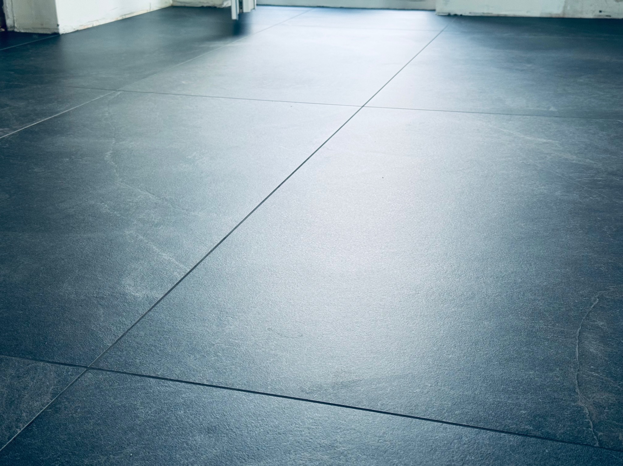 Ułożone, szare płytki podłogowe z wąską fugą w jasnym pomieszczeniu. Widok z góry na gładką powierzchnię. Minimalistyczny design.