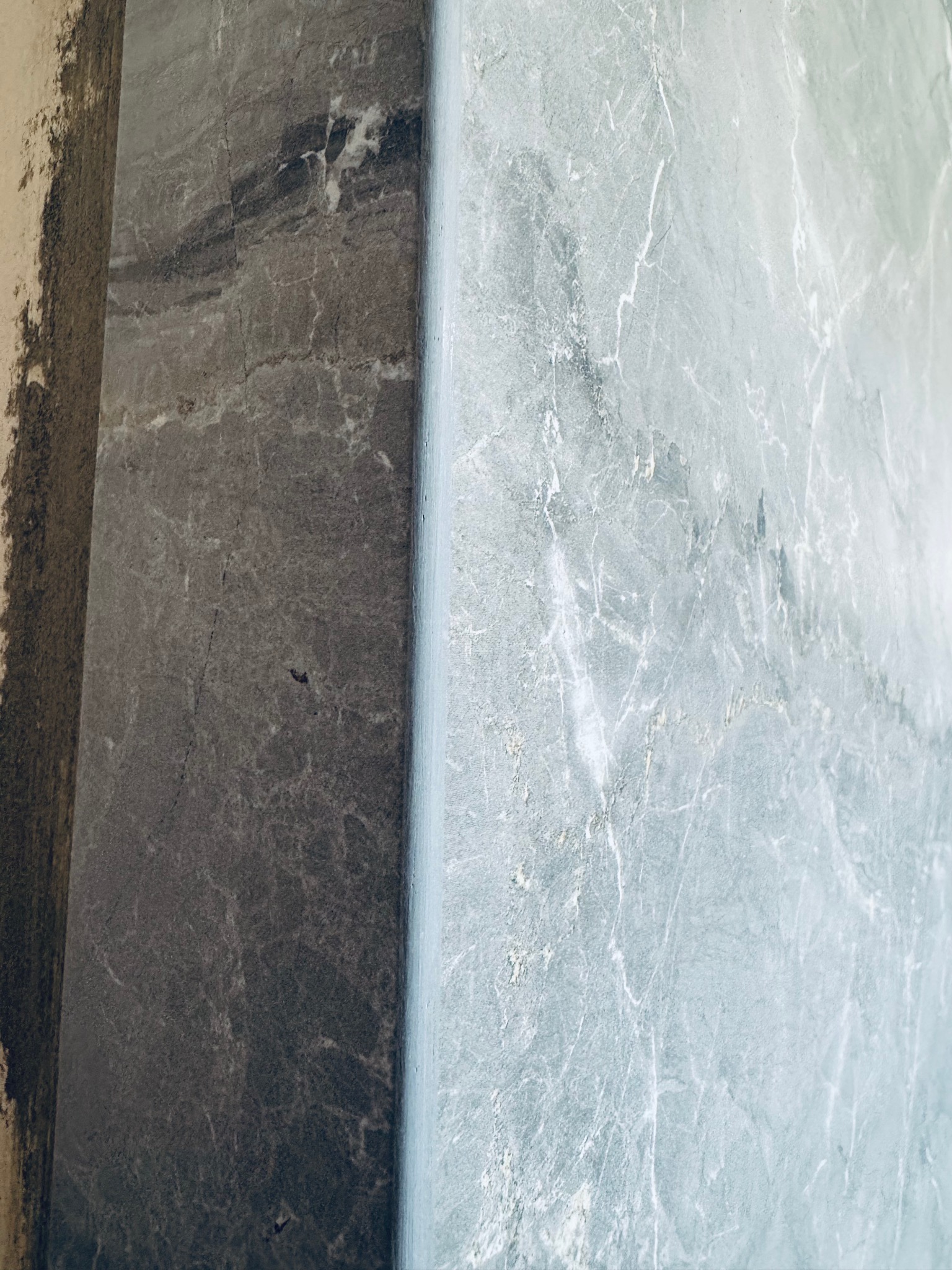 Położona płytka imitująca marmur w odcieniach szarości i błękitu, widoczny fragment ściany przed wykończeniem. Detal wykończenia wnętrza.