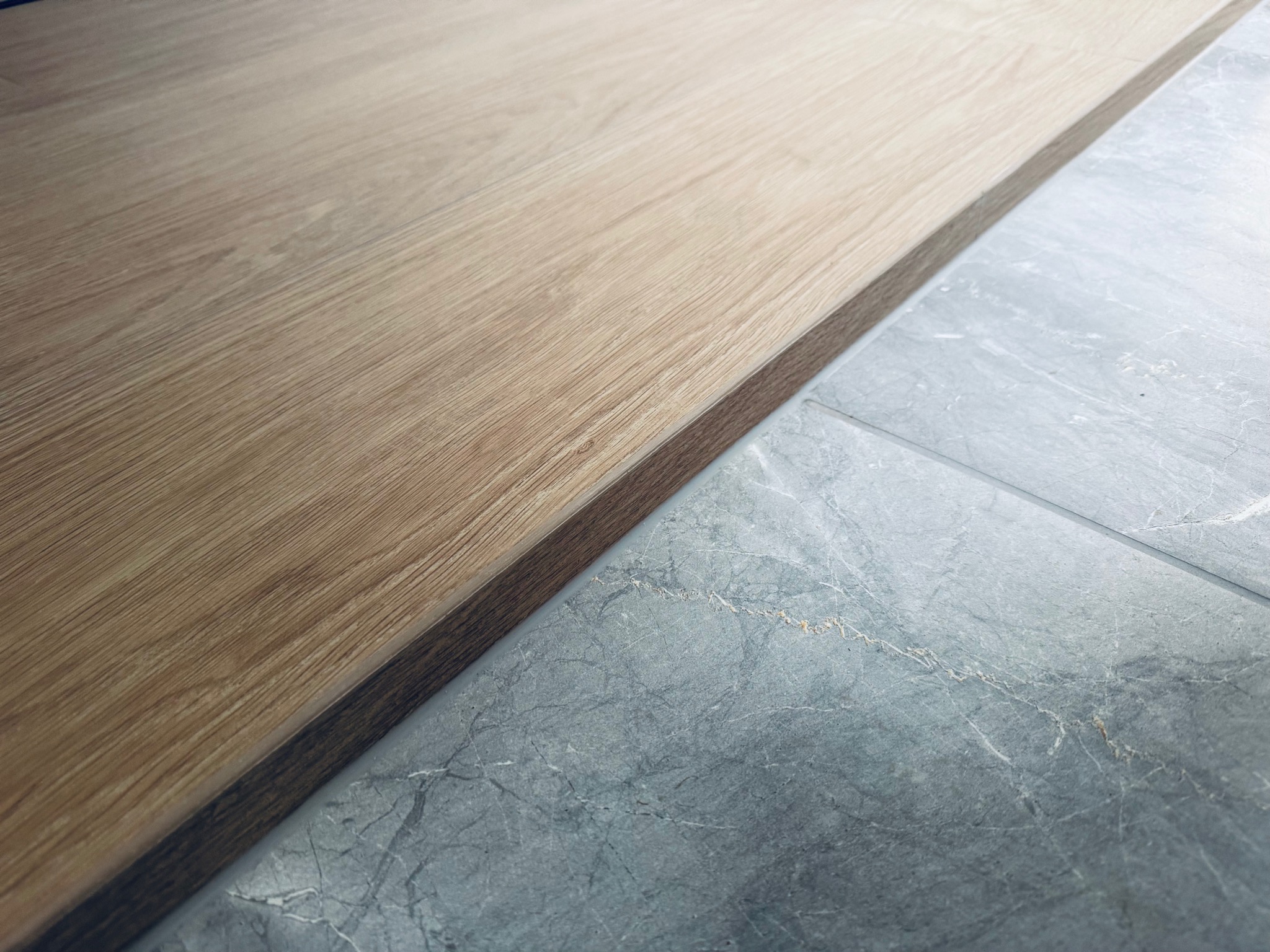 Połączenie podłogi: panel drewnopodobny i szara płytka imitująca marmur. Widok z góry, bliskie ujęcie, ukazujące detale materiałów i precyzję wykonania.