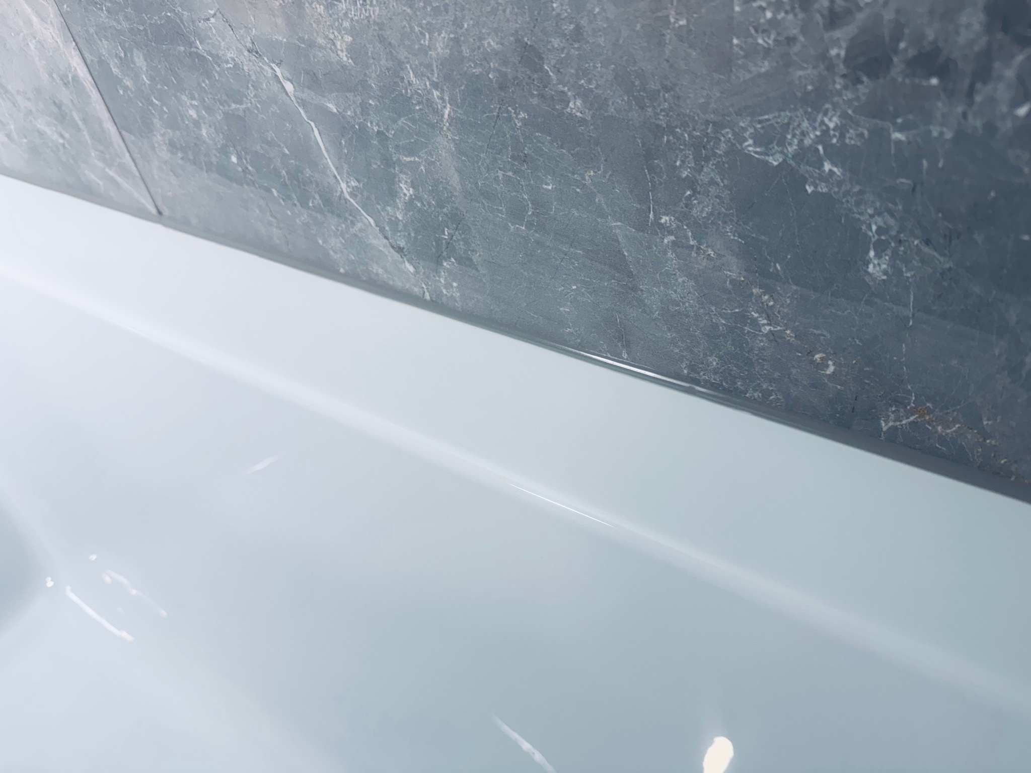 Fragment wykończonej łazienki: biała wanna z szarą, marmurkową okładziną ścienną. Minimalistyczny design, czyste linie, nowoczesne wykończenie.