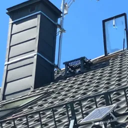 Antena TV, panel solarny i komin na dachu krytym dach&oacute;wką w słoneczny dzień. Widoczne zabezpieczenia przeciwśniegowe.