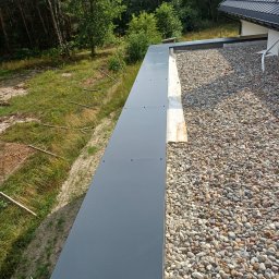 ASSAMAH-VH Vasyl Habiak - Płaski dach pokryty drobnymi kamieniami, zabezpieczony szarą, metalową obróbką blacharską. Widok z góry na krawędź dachu i otaczającą zieleń.