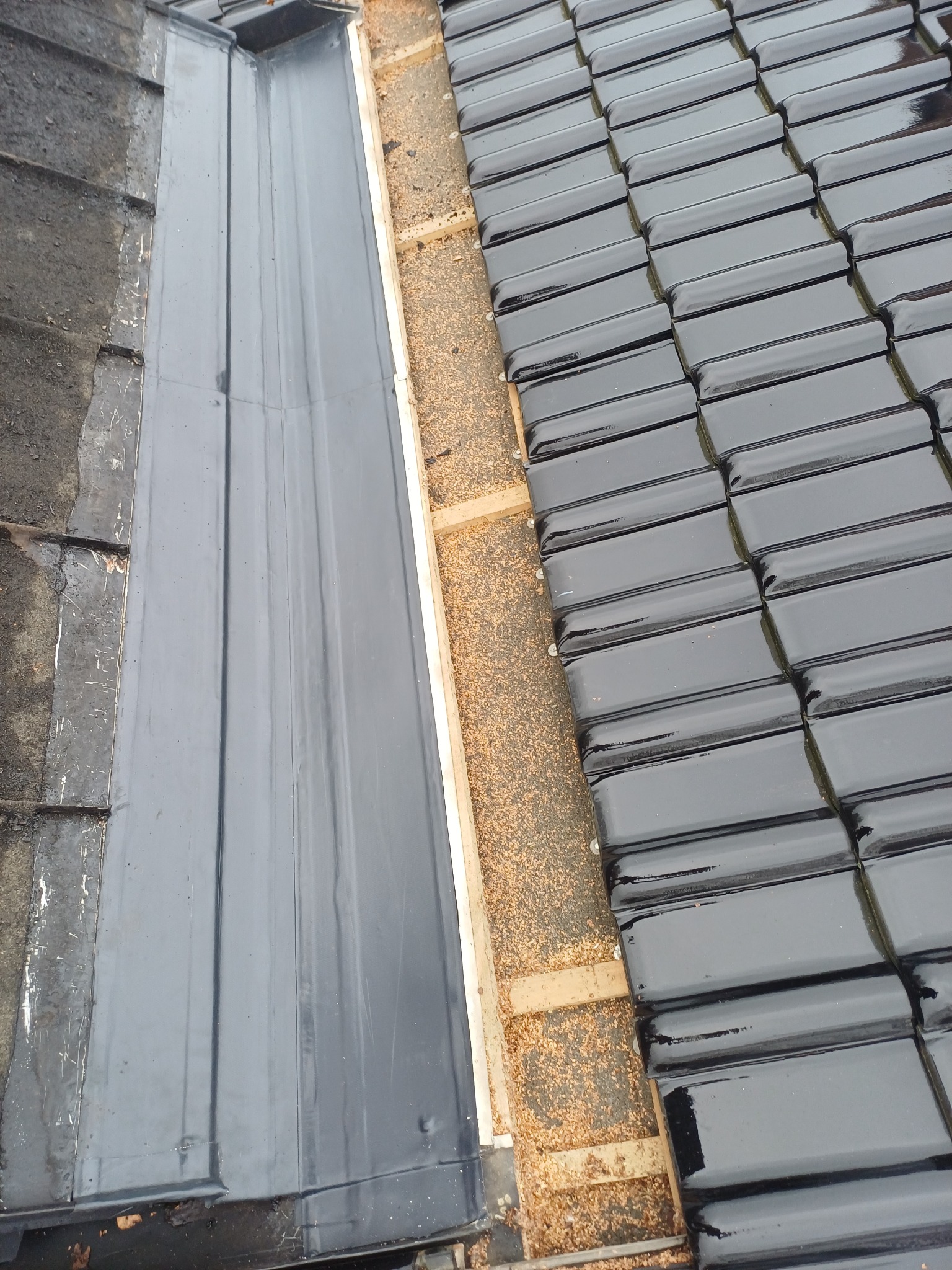 Szczegółowe ujęcie dachu z czarną dachówką i elementami rynny, ukazujące detale konstrukcyjne i materiały użyte w systemie odprowadzania wody.