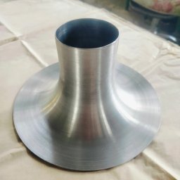 ROSIK JUSTYNA I JÓZEF SP.C. GALWANOTECHNIKA-LAMPY I AKCESORIA DO POWOZÓW KONNYCH,PONIEC - Metalowy element o kształcie stożka z kołnierzem, wykonany z polerowanego metalu. Widoczne ślady obróbki na powierzchni.  Zdjęcie z bliska, na neutralnym tle.