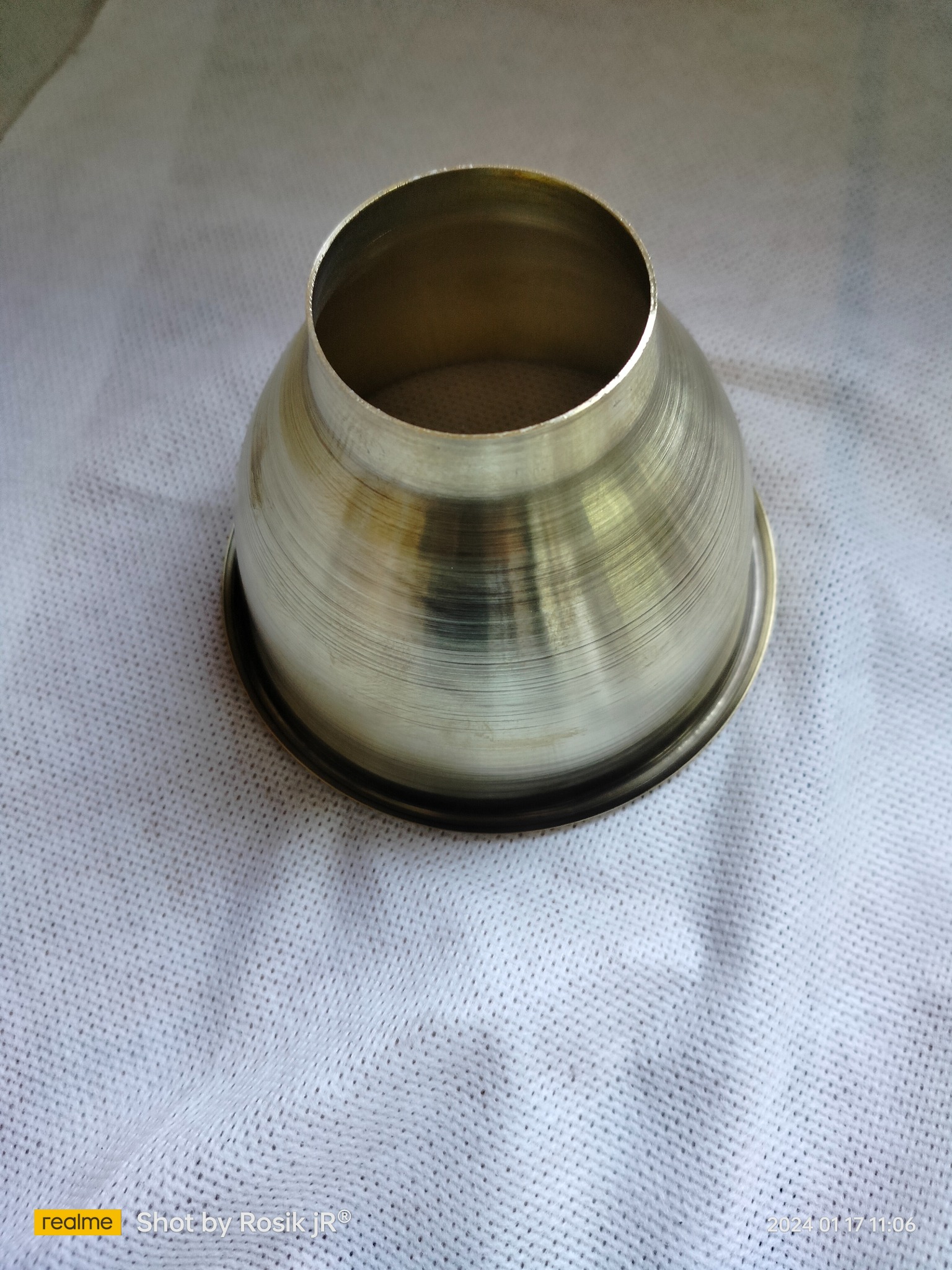 Metalowy element w kształcie stożka ze śladami obróbki, na białym tle. Widoczne delikatne rysy i refleksy świetlne na powierzchni metalu.