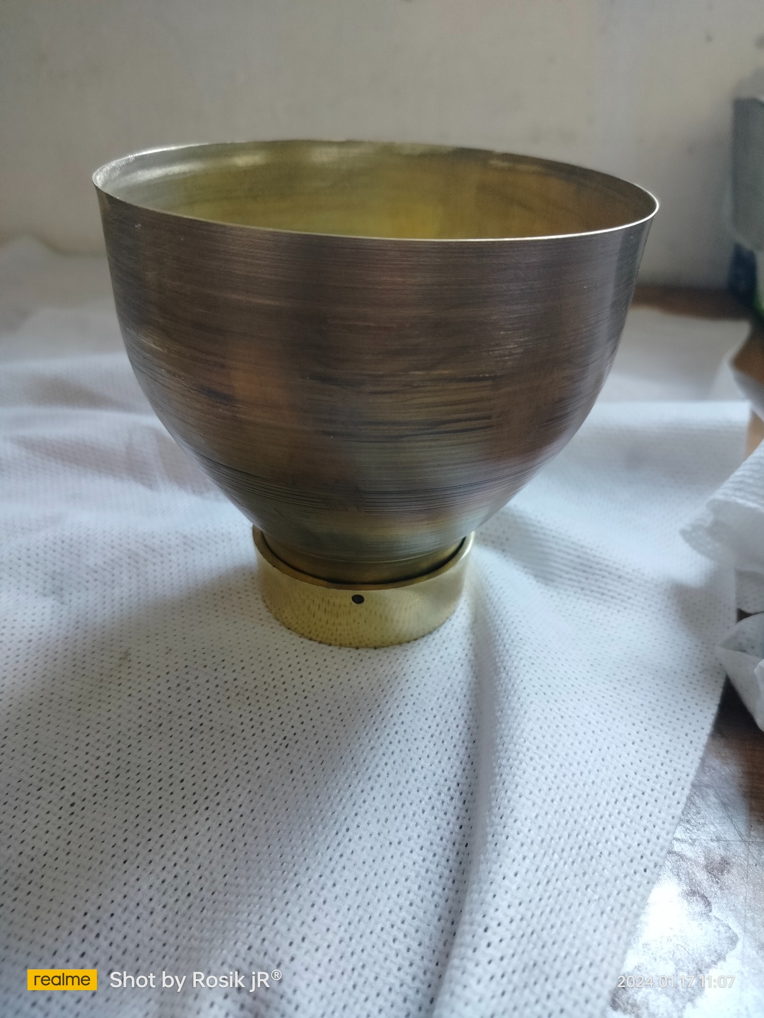 Miedziana misa z podstawą na białej ściereczce. Misa ma delikatne, poziome ślady po obróbce. Wnętrze misy jest jaśniejsze, w odcieniu złota.