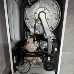 Otwarty piec gazowy Viessmann, widoczne elementy wewnętrzne: palnik, wymiennik ciepła, elektronika. Biała obudowa, szare tło. Detaliczny widok wnętrza.