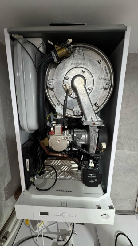 Otwarty piec gazowy Viessmann, widoczne elementy wewnętrzne: palnik, wymiennik ciepła, elektronika. Biała obudowa, szare tło. Detaliczny widok wnętrza.