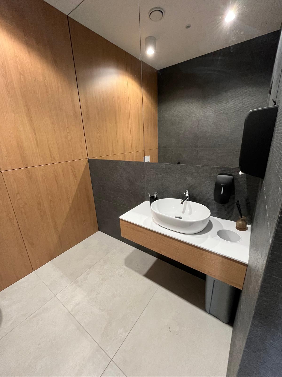 Nowoczesna łazienka z drewnianą okładziną ścienną i szarą płytką, owalna umywalka na blacie, minimalistyczny design, eleganckie wykończenie.