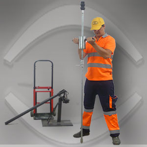 Pracownik w odblaskowej odzieży obsługuje sondę geologiczną na tle sprzętu do badań gruntu, w żółtej czapce z logo firmy. Badanie geotechniczne gruntu.