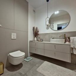 R Design Meble Na Wymiar - Nowoczesna łazienka z wiszącą toaletą, szafką z umywalką nablatową i okrągłym lustrem podwieszonym na dekoracyjnym kablu.