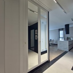 R Design Meble Na Wymiar - Elegancka szafa wnękowa z lustrzanymi drzwiami odbija wnętrze nowoczesnej kuchni z wyspą i parkietem w jodełkę, tworząc wrażenie przestronności.