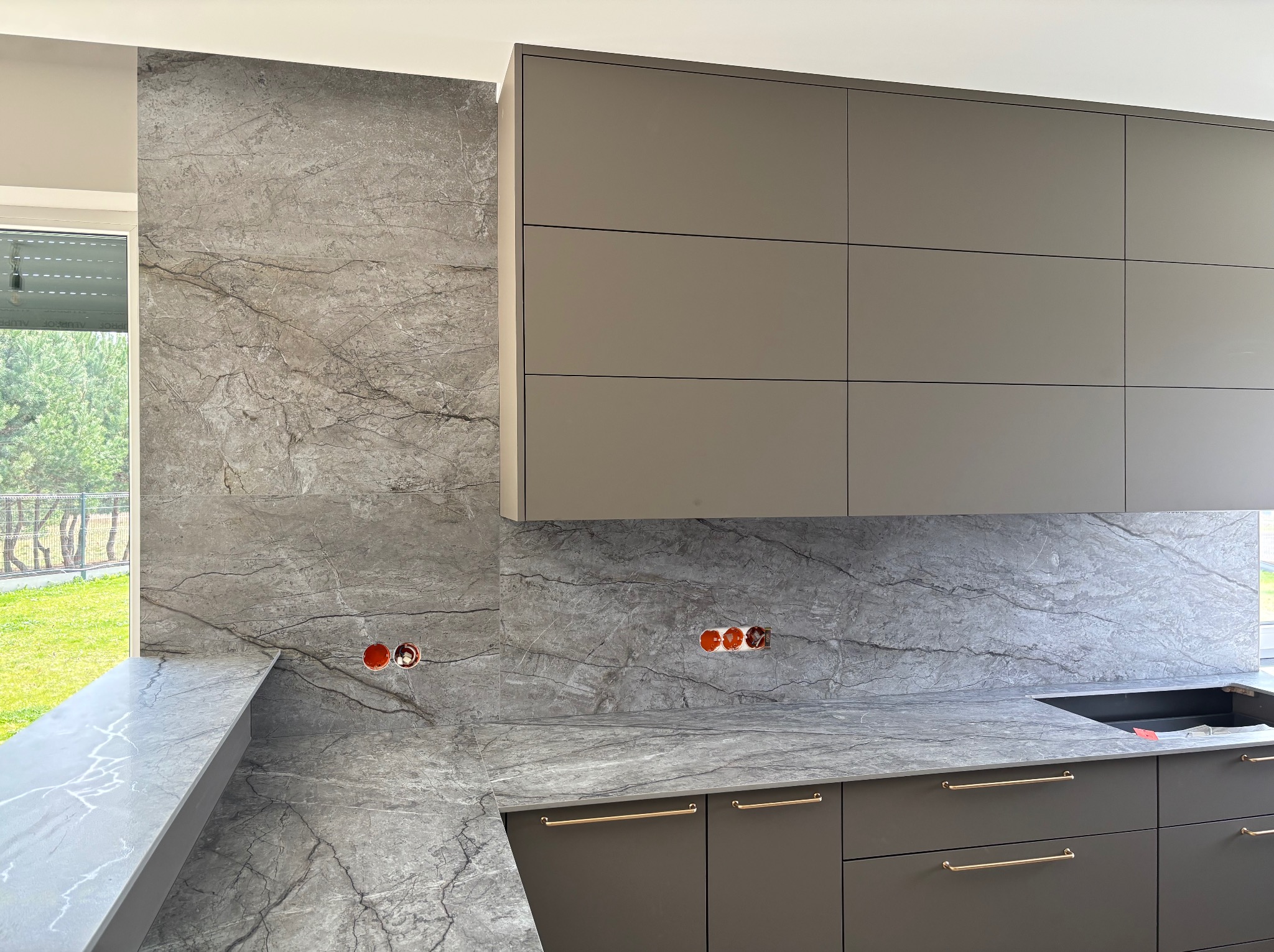 Szary blat kamienny z marmurowym wzorem w nowoczesnej kuchni, z widocznymi gniazdkami elektrycznymi i elementami zabudowy kuchennej w szarości.