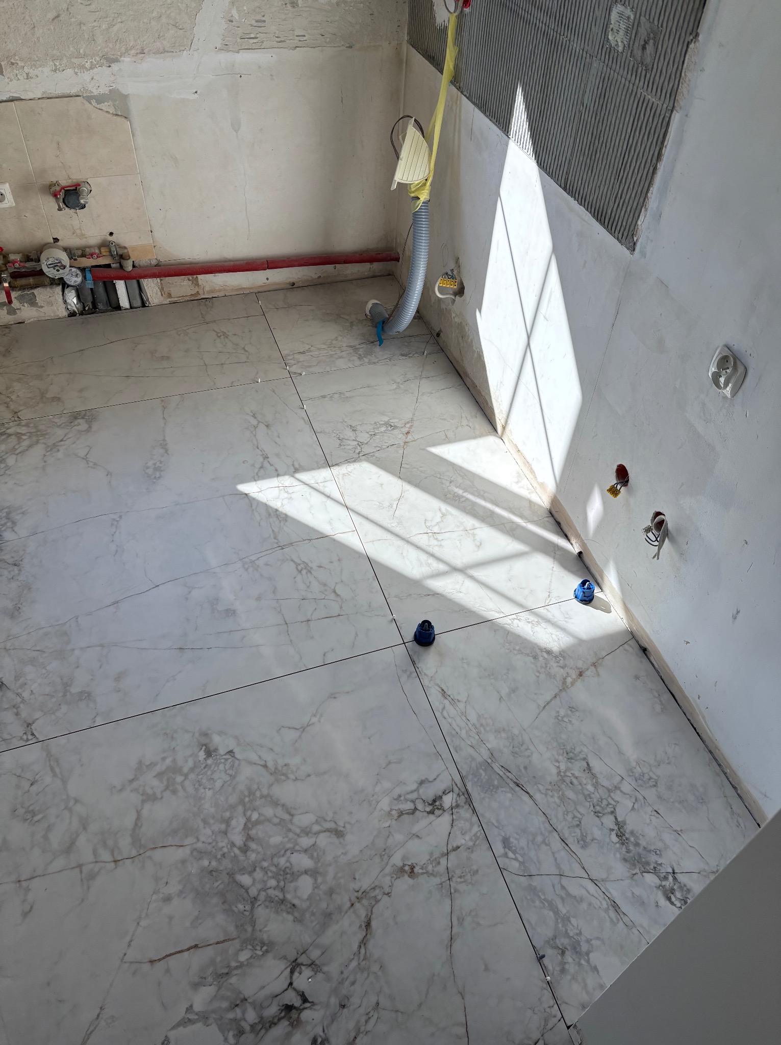 Białe płytki imitujące marmur na podłodze w trakcie remontu łazienki, widoczne nieotynkowane ściany i instalacje.