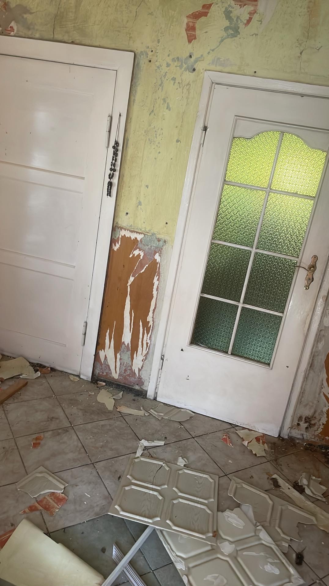 Wnętrze w trakcie demontażu w Gubinie: zerwane tapety, uszkodzone płytki podłogowe, dwie białe drzwi. Przygotowanie do remontu.