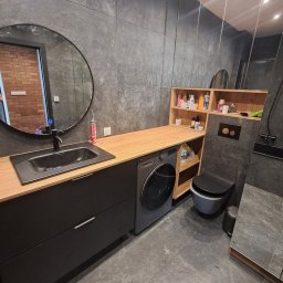 FACH EKSPERT JACEK KUSKA - Nowoczesna łazienka w Tychach z szarą płytką, drewnianym blatem, okrągłym lustrem i pralką pod blatem. Minimalistyczny design, oświetlenie sufitowe.