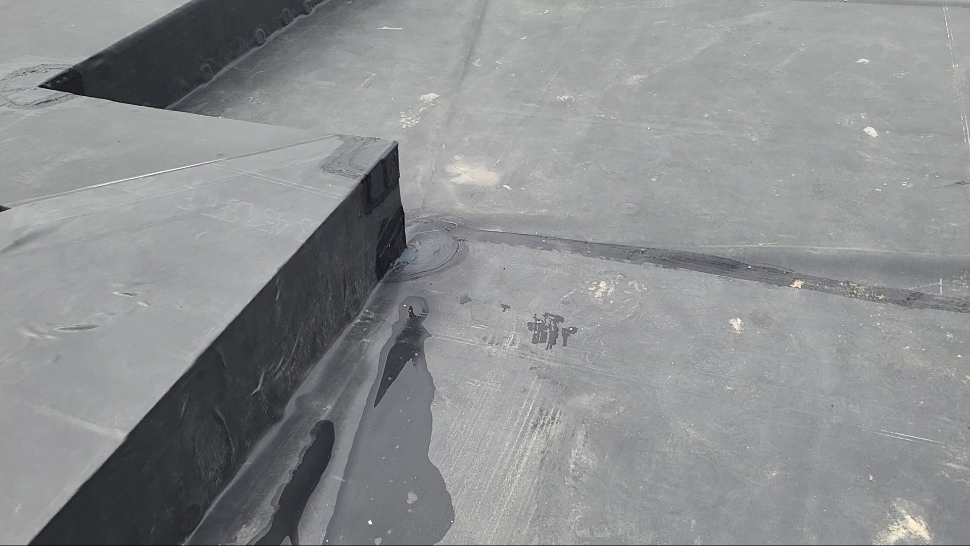 Szczegółowe ujęcie płaskiego dachu z papy bitumicznej, ukazujące łączenia i detale wykończenia, z widocznymi śladami wilgoci i zabrudzeń.