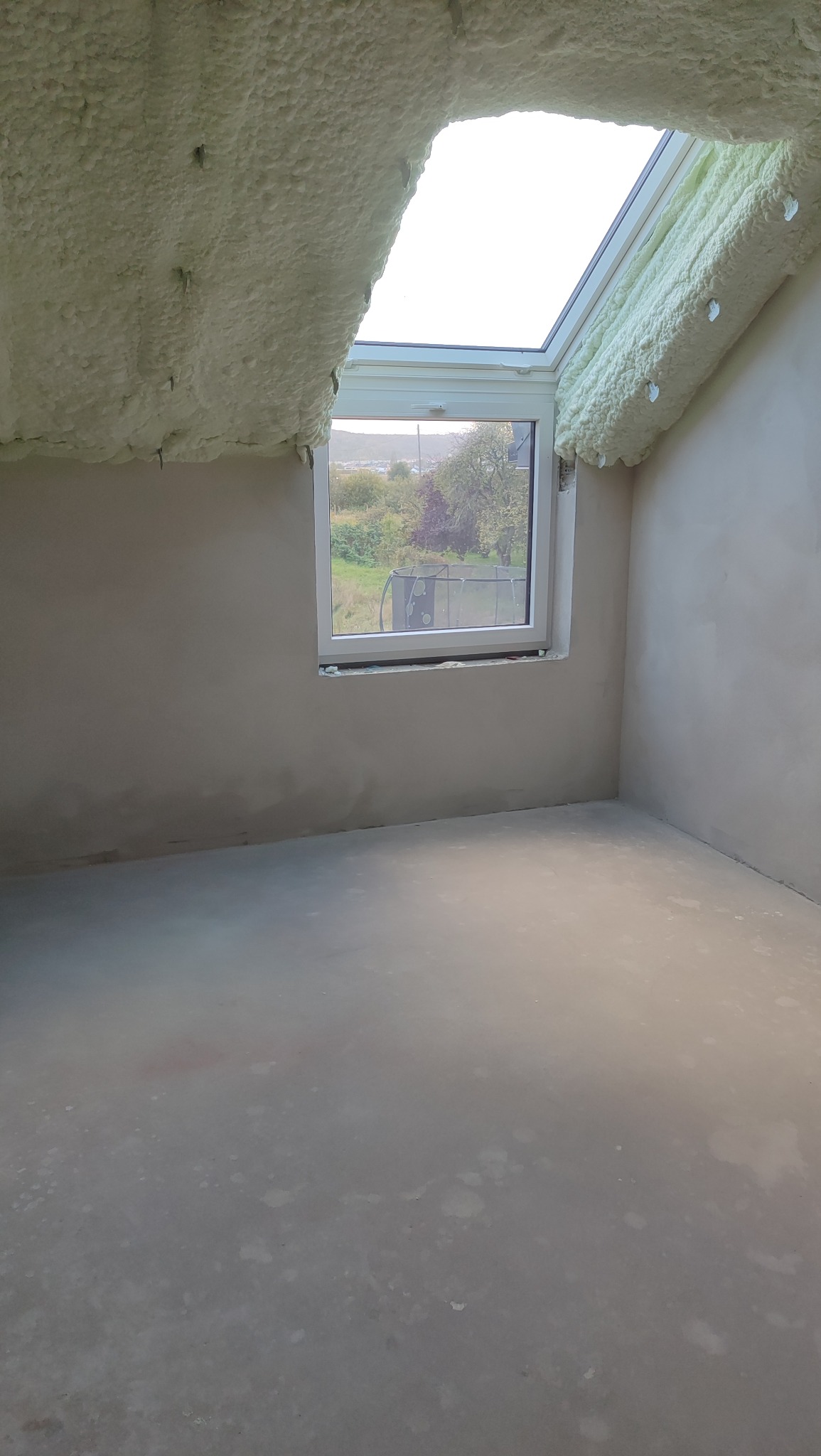 Poddasze po ociepleniu pianką PUR, widoczne okno dachowe i fragment ściany. Pianka pokrywa skosy dachu, tworząc jednolitą warstwę izolacyjną.