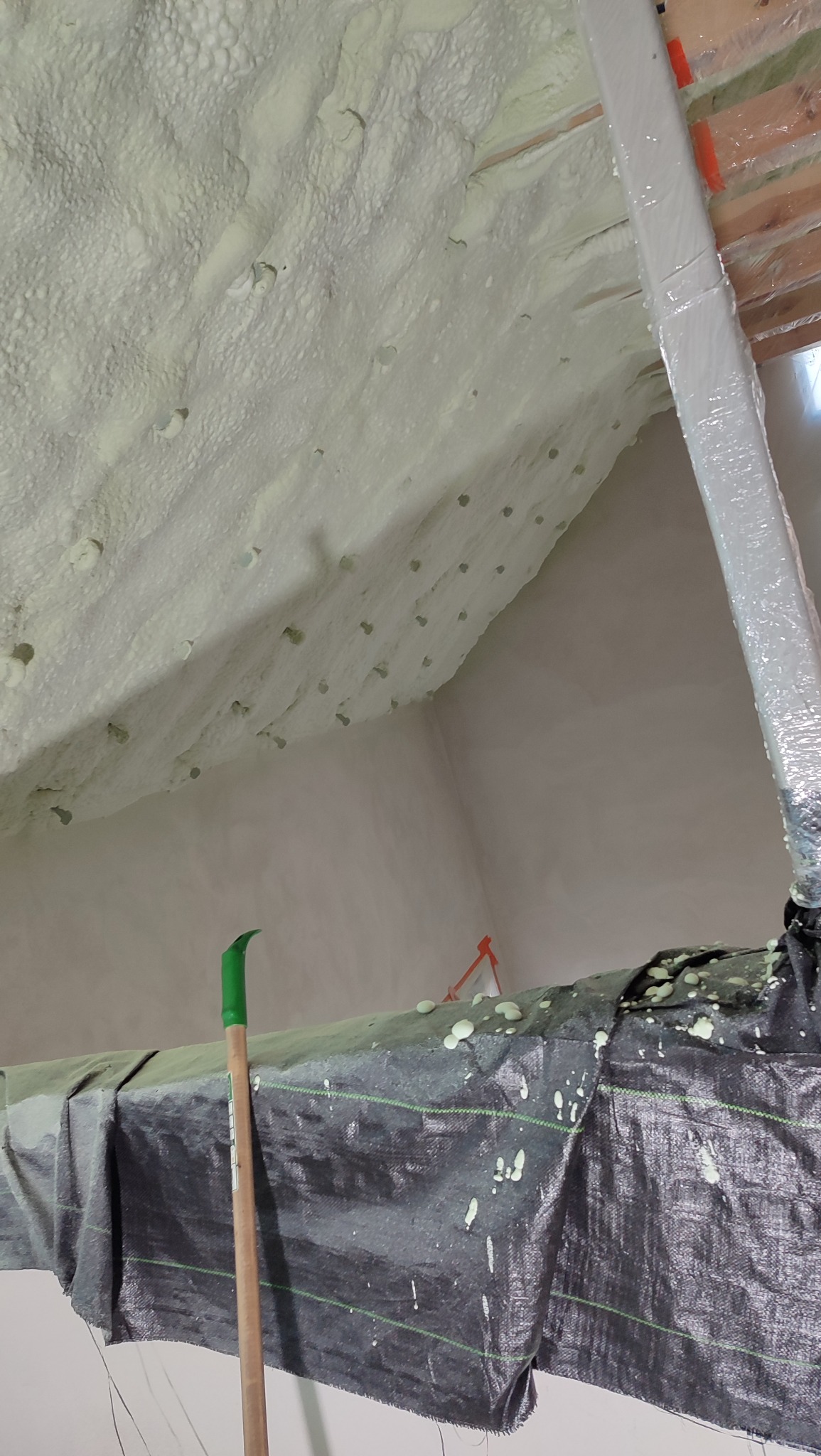 Poddasze po ociepleniu pianką PUR z widocznym narzędziem i zabezpieczeniem. Izolacja natryskowa na skośnym dachu, detale pianki i konstrukcji drewnianej.