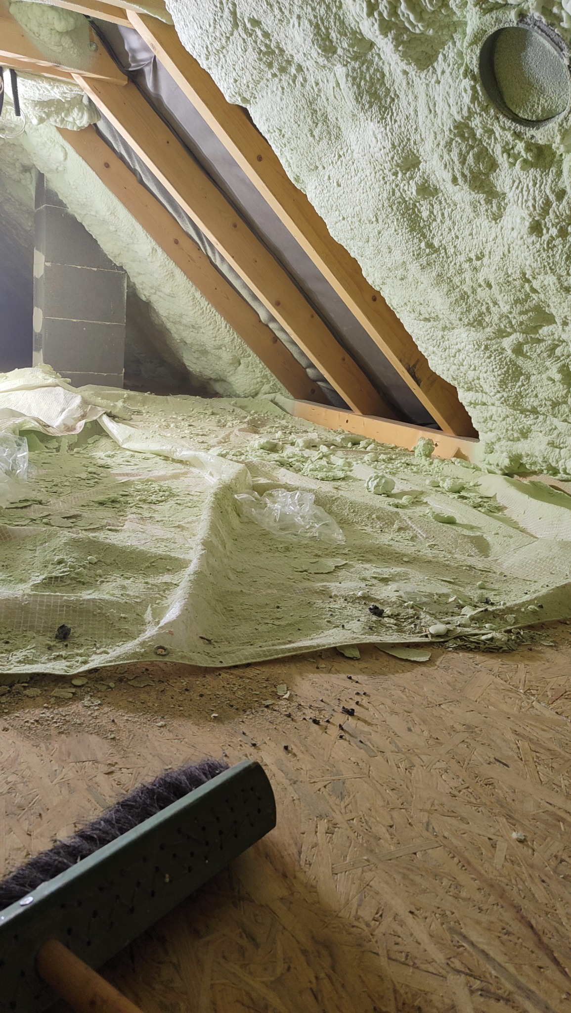 Poddasze po ociepleniu pianką PUR, widoczne drewniane elementy konstrukcyjne i fragment podłogi z leżącą szczotką. Na podłodze resztki pianki i folii ochronnej.