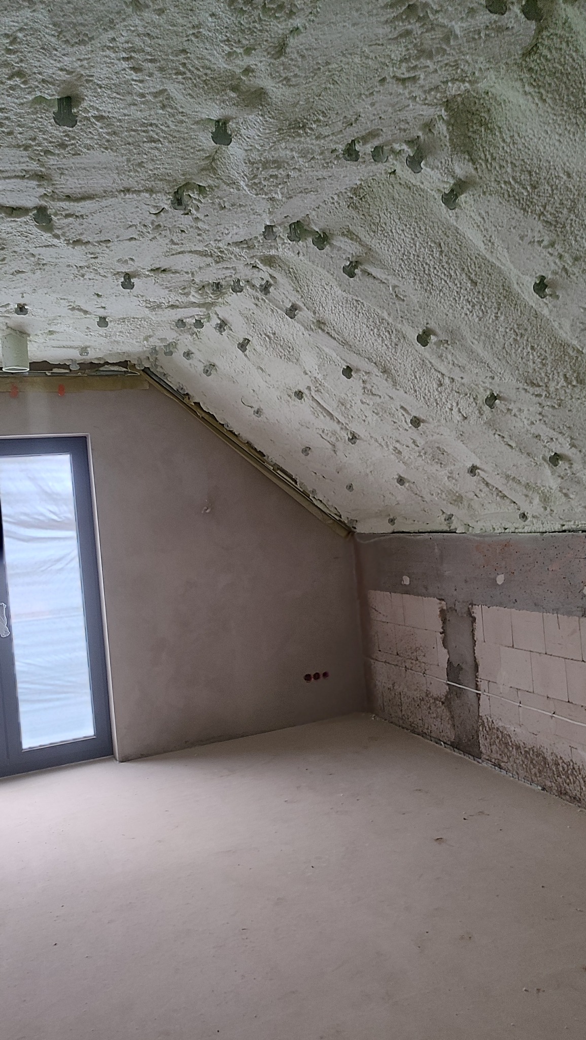 Poddasze po ociepleniu pianką PUR, widoczne mocowania, ściany w stanie surowym, okno. Realizacja ocieplenia poddasza z bliska.