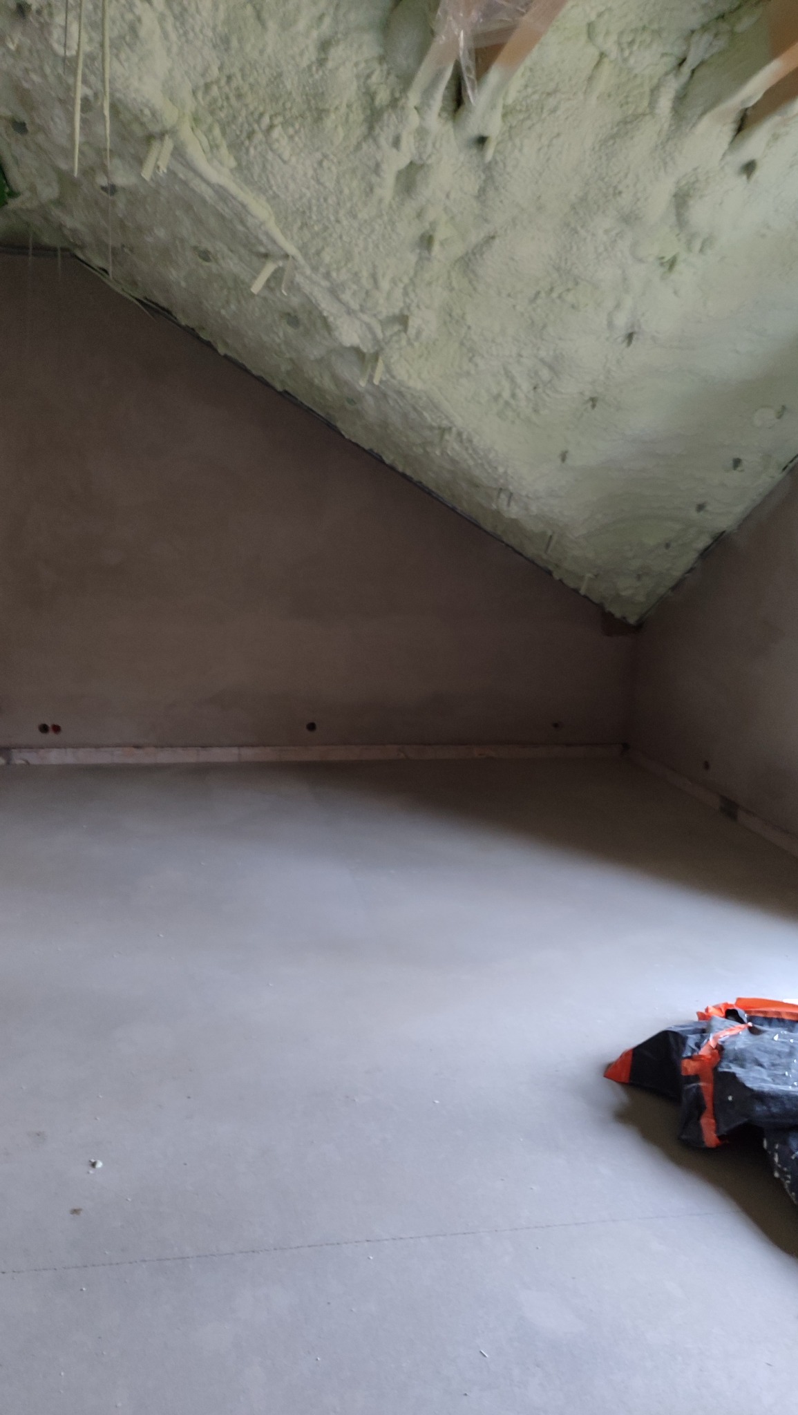 Poddasze po ociepleniu pianką PUR, widoczne fragmenty drewnianej konstrukcji. Ściany otynkowane, na podłodze folia ochronna. Ujęcie z dołu, szeroki kadr.