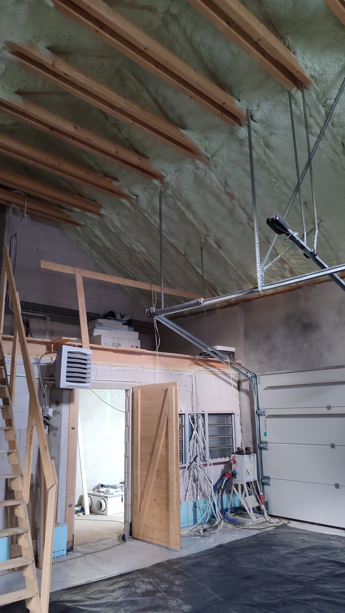 Poddasze garażu po ociepleniu pianką PUR, widoczne drewniane belki stropowe i metalowe elementy konstrukcyjne. Otwarta przestrzeń z widoczną instalacją elektryczną.