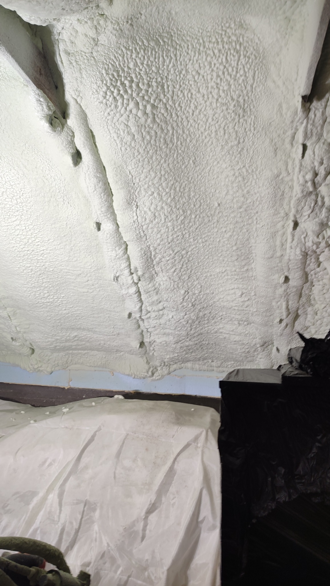 Poddasze po ociepleniu pianką PUR, widoczne nierówności i struktura piany. Częściowo zakryte folią ochronną, z fragmentami drewnianej konstrukcji.