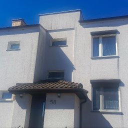 Warm-home - Fasada budynku z numerem 58 w słoneczny dzień. Widoczne okna z roletami, biała elewacja z fakturą tynku oraz fragment dachu. Błękitne niebo w tle.