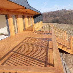 BORO KRZYSZTOF BOROWY - Nowoczesny taras drewniany z balustradą i schodami, przylegający do budynku z drewnianą elewacją i dużymi oknami. Widok na wzgórze w tle.